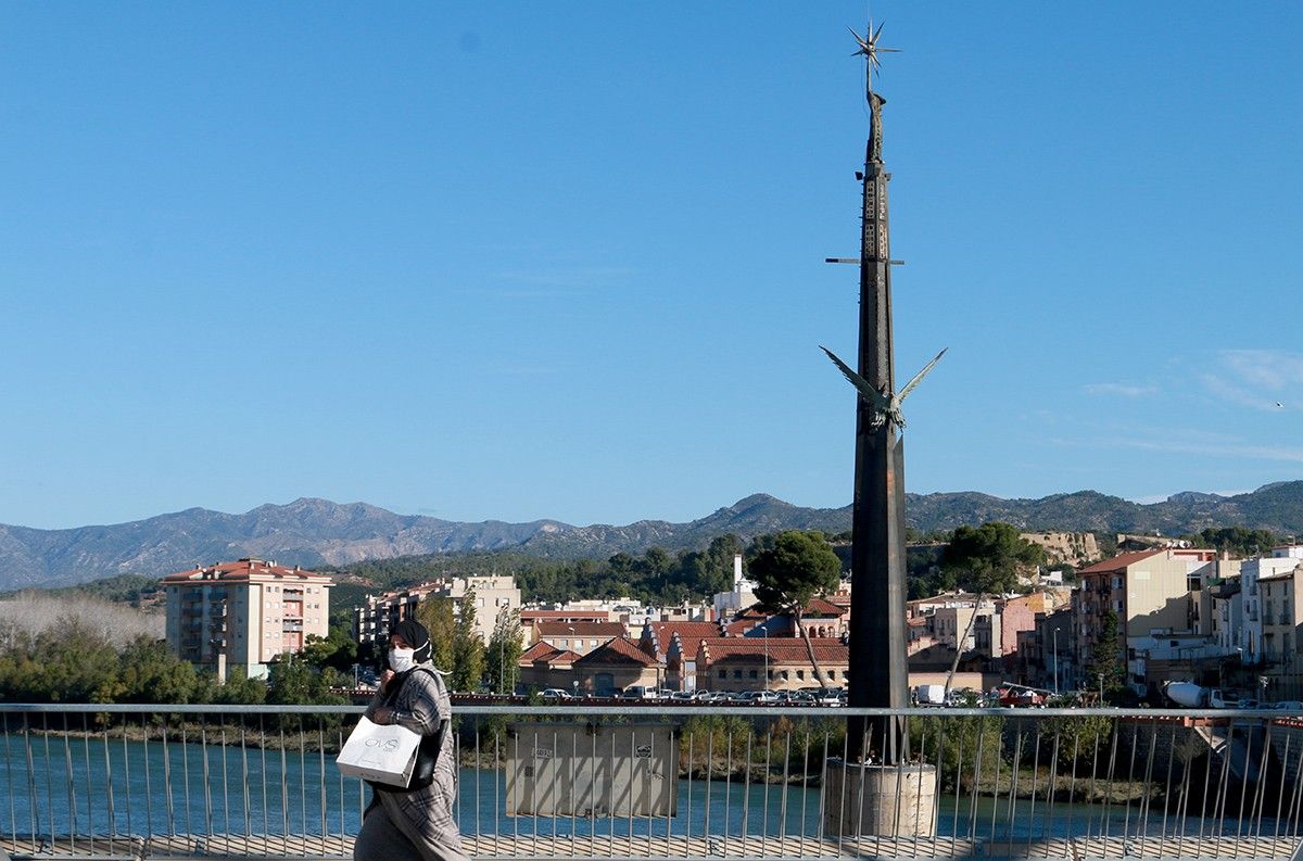 Una vianant camina pel pont de l'Estat de Tortosa. Al fons, el monument franquista.