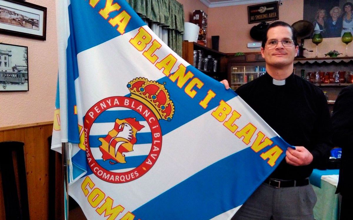 El capellà exhibint la bandera blanc-i-blava de l'Espanyol, el seu equip.