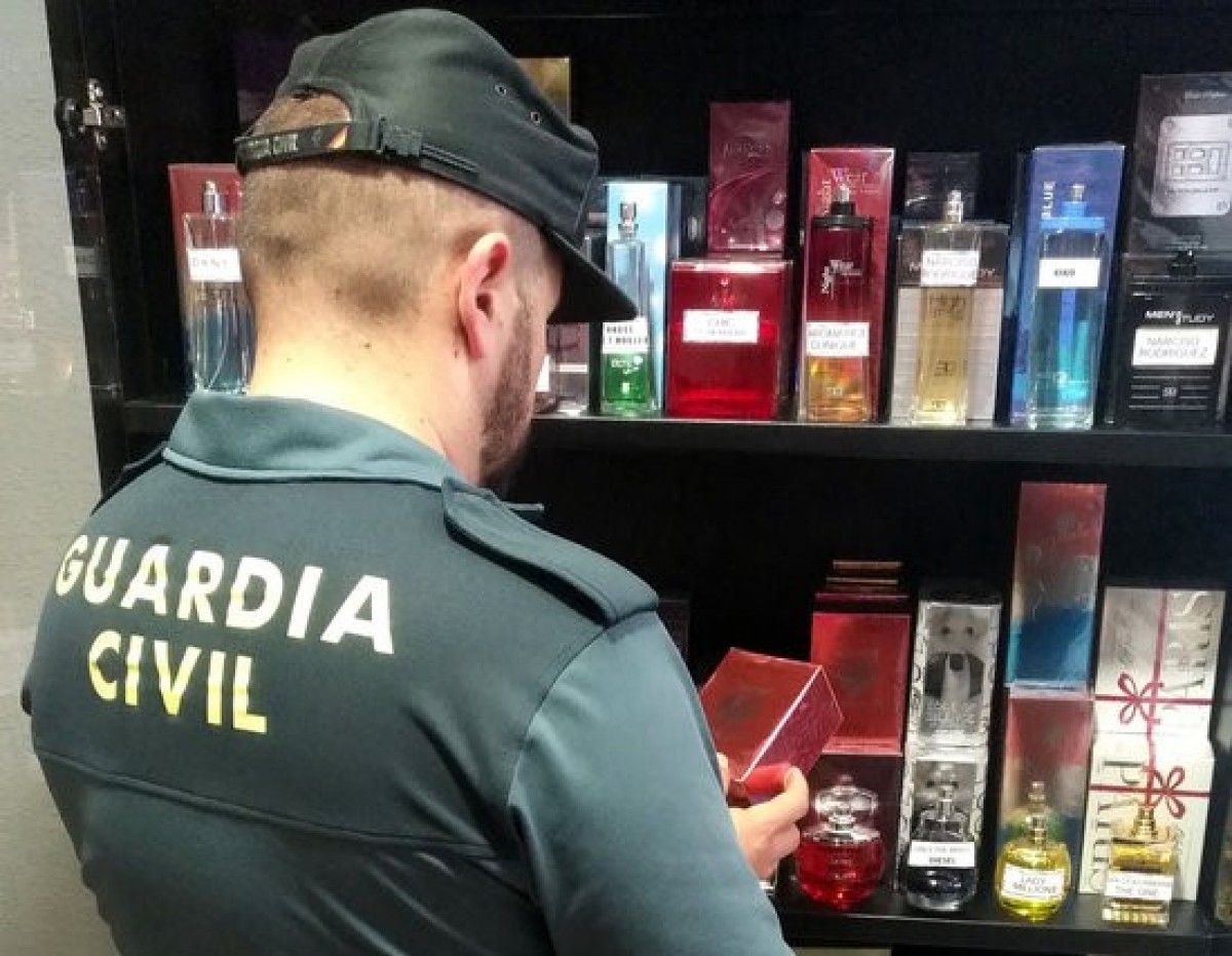 Un agent de la Guàrdia Civil mirant una ampolla de perfum falsificat davant d'una estanteria
