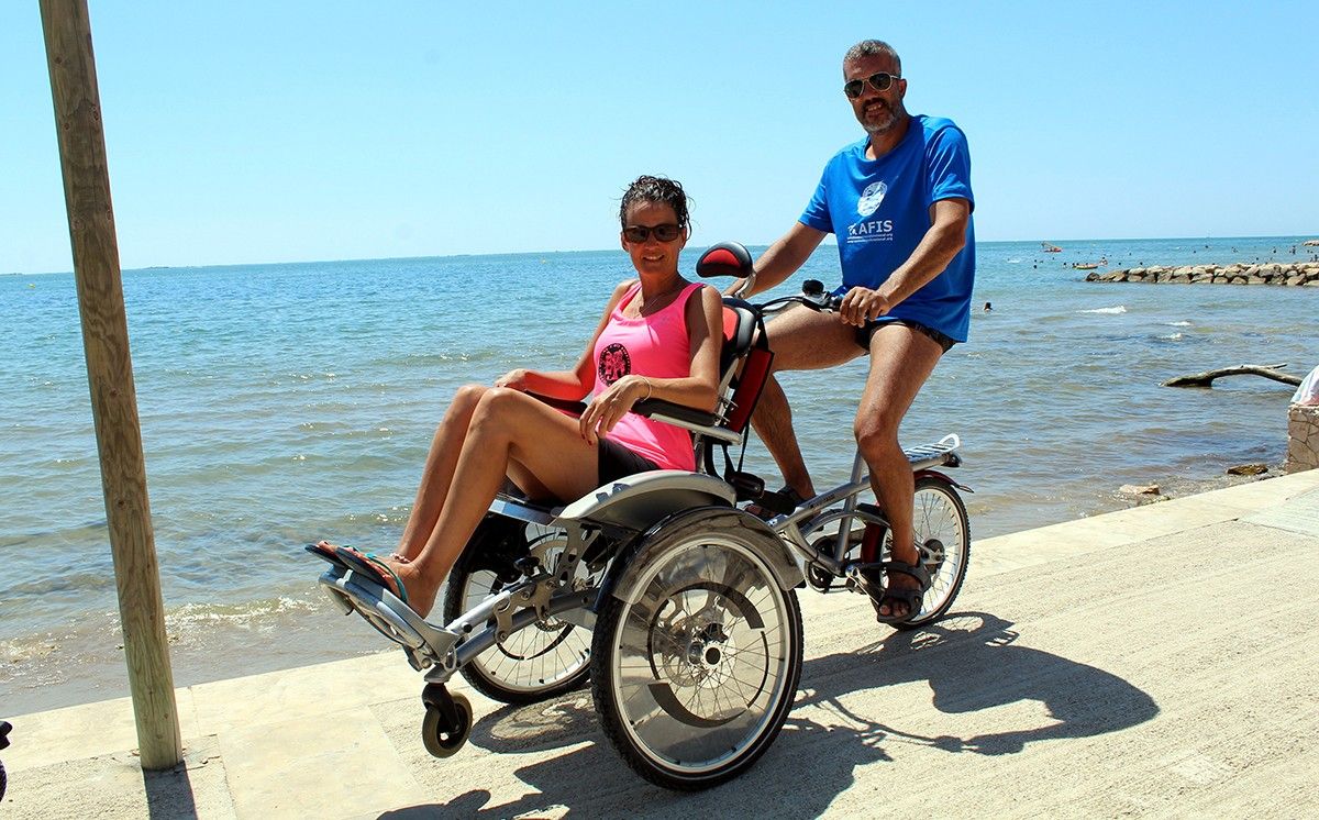 Una parella passeja prop de la platja amb una cadira-bicicleta adaptada OPair.