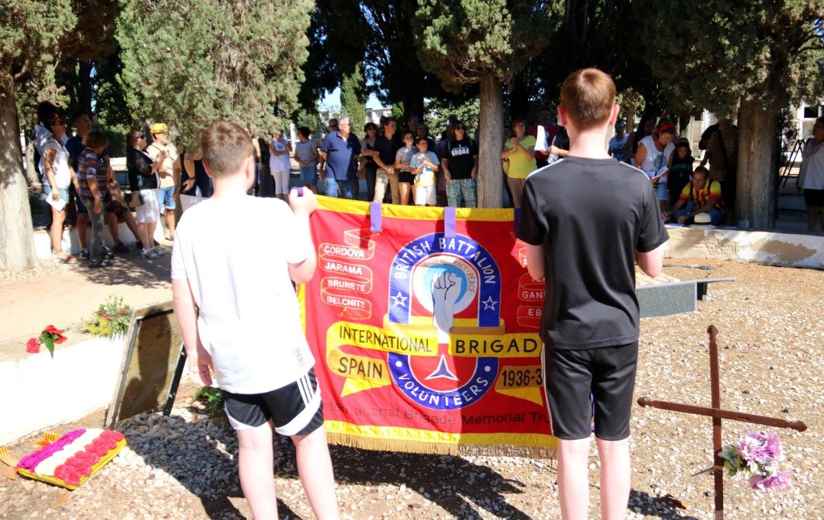 Dos joves familiars dels brigadistes britànics portant una bandera de l'entitat IBMT durant l'homenatge a la fossa comuna del cementiri del Perelló.