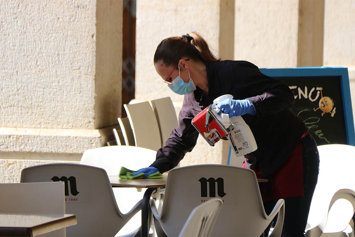 La propietària d'un bar de Tortosa netejant una taula de la terrassa.