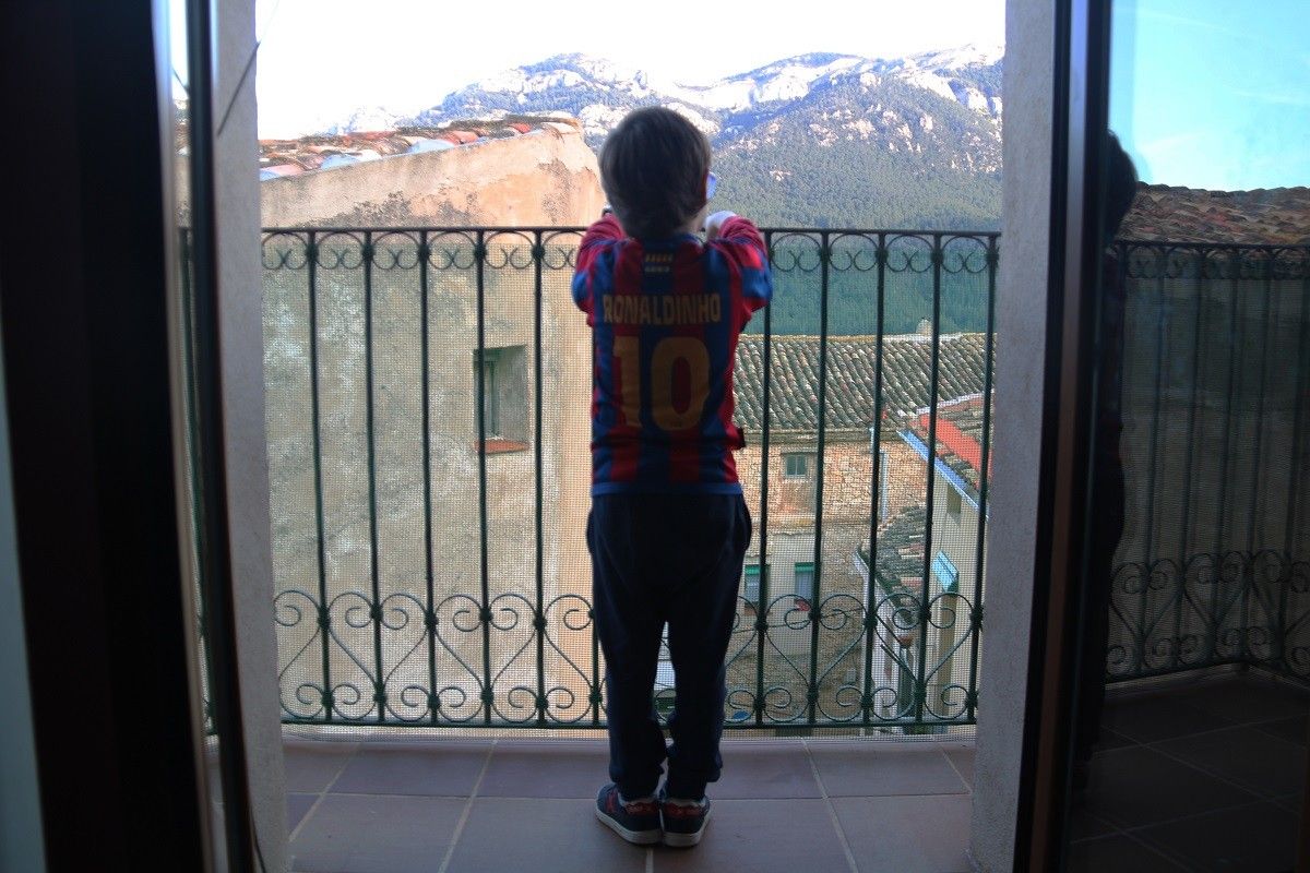 Un nen observant des del balcó de casa l'entorn natural del seu municipi, durant el confinament