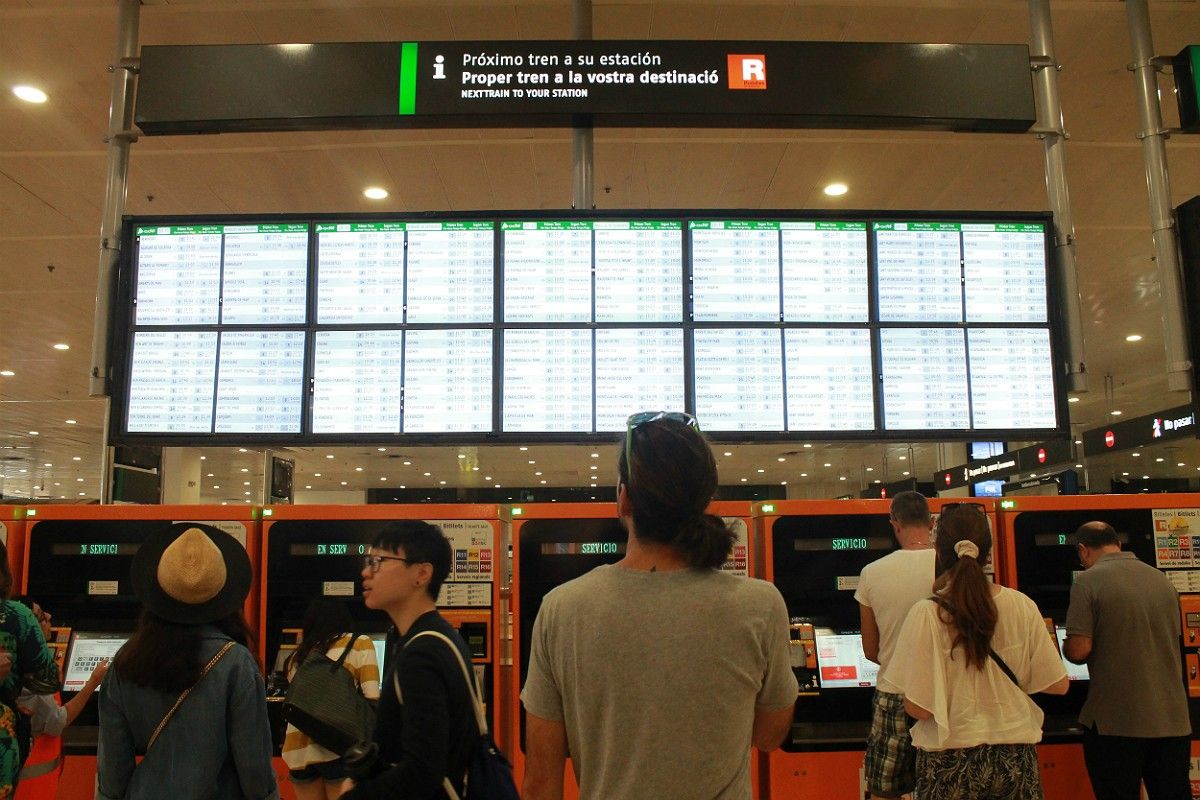 Un grup d'usuaris de Rodalies, majoritàriament turistes, observa les pantalles d'informació de l'estació de Sants durant la vaga del 12 de juny