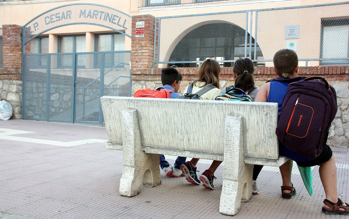 Quatre xiquets esperen asseguts a un banc a les portes de l'escola César Martinell del Pinell de Brai.