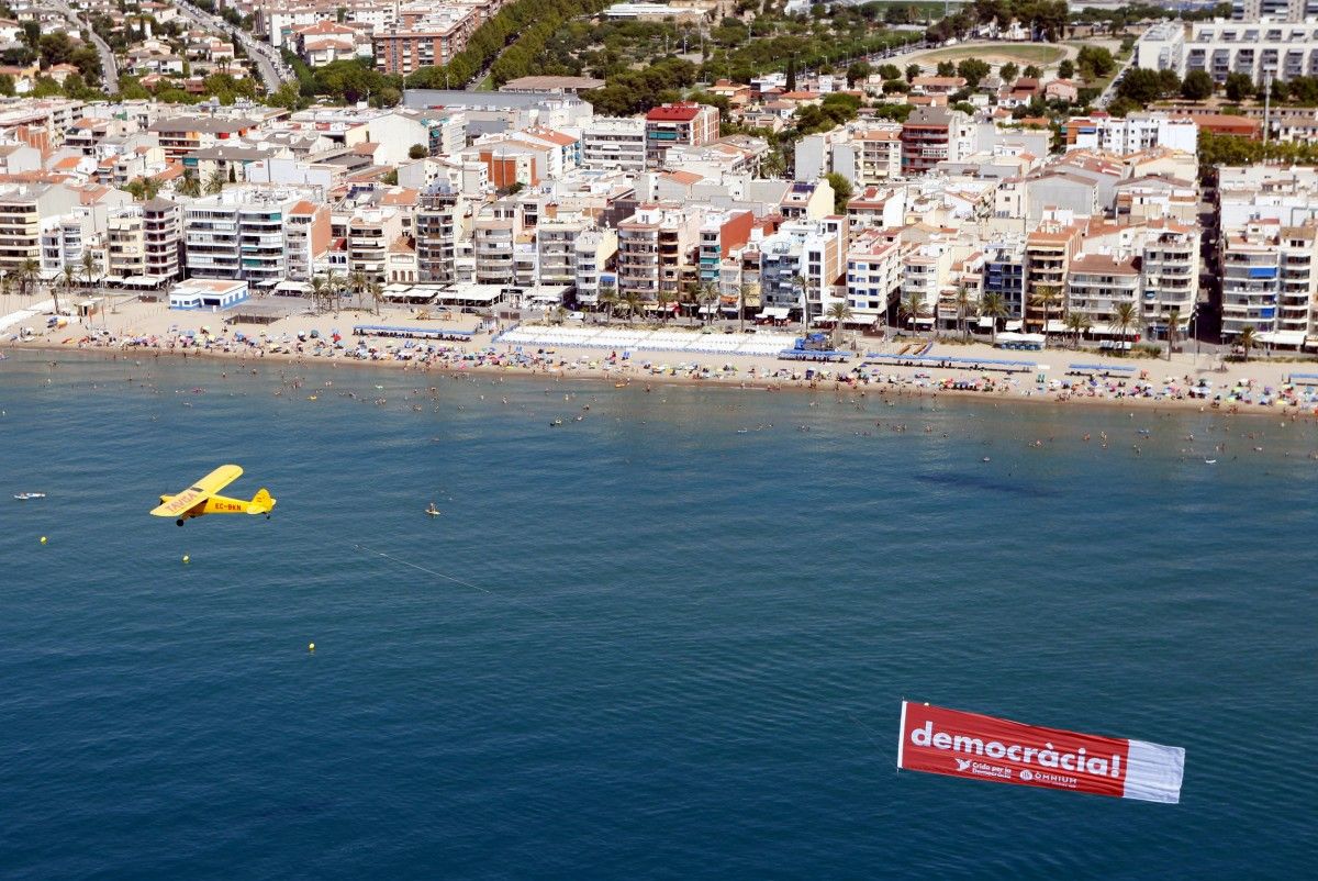 Imatge de l'avioneta amb la pancarta on es pot llegir 'democràcia' sobrevolant una platja catalana