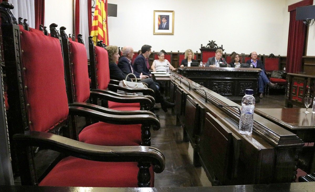 En primer pla les cadires buides dels regidors socialistes, al fons, la paret de la sala de plens sense la foto oficial de Felip VI. 