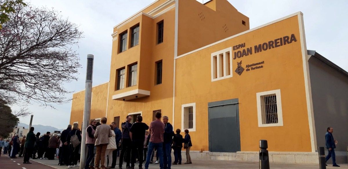 Desenes de persones esperen a l'entrada del nou Espai Joan Moreira de Ferreries, a Tortosa, per veure el resultat de la transformació de les antigues naus industrials en un equipament cultural i social  